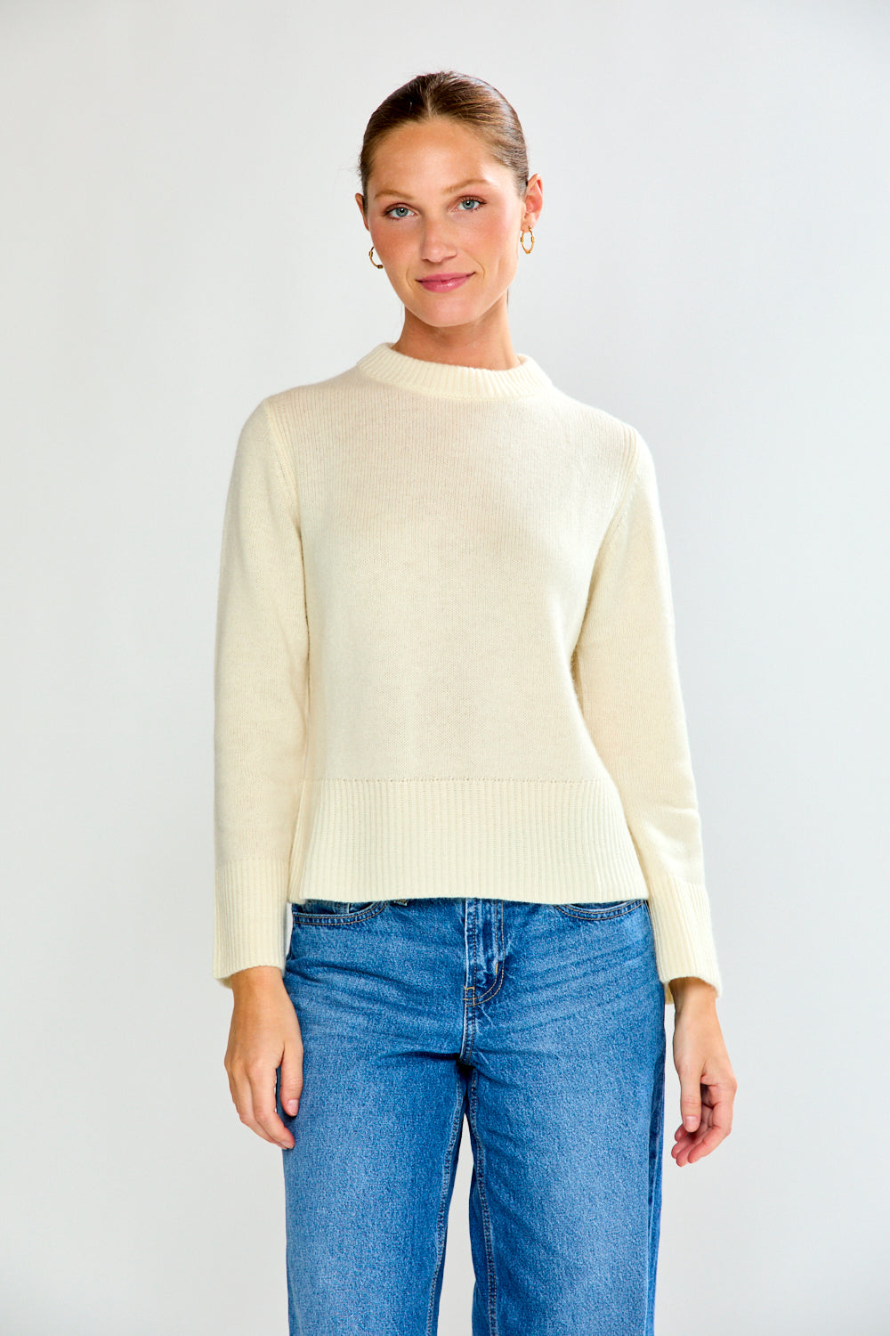 Woman wearing a cream sweater and blue jeans against a white background