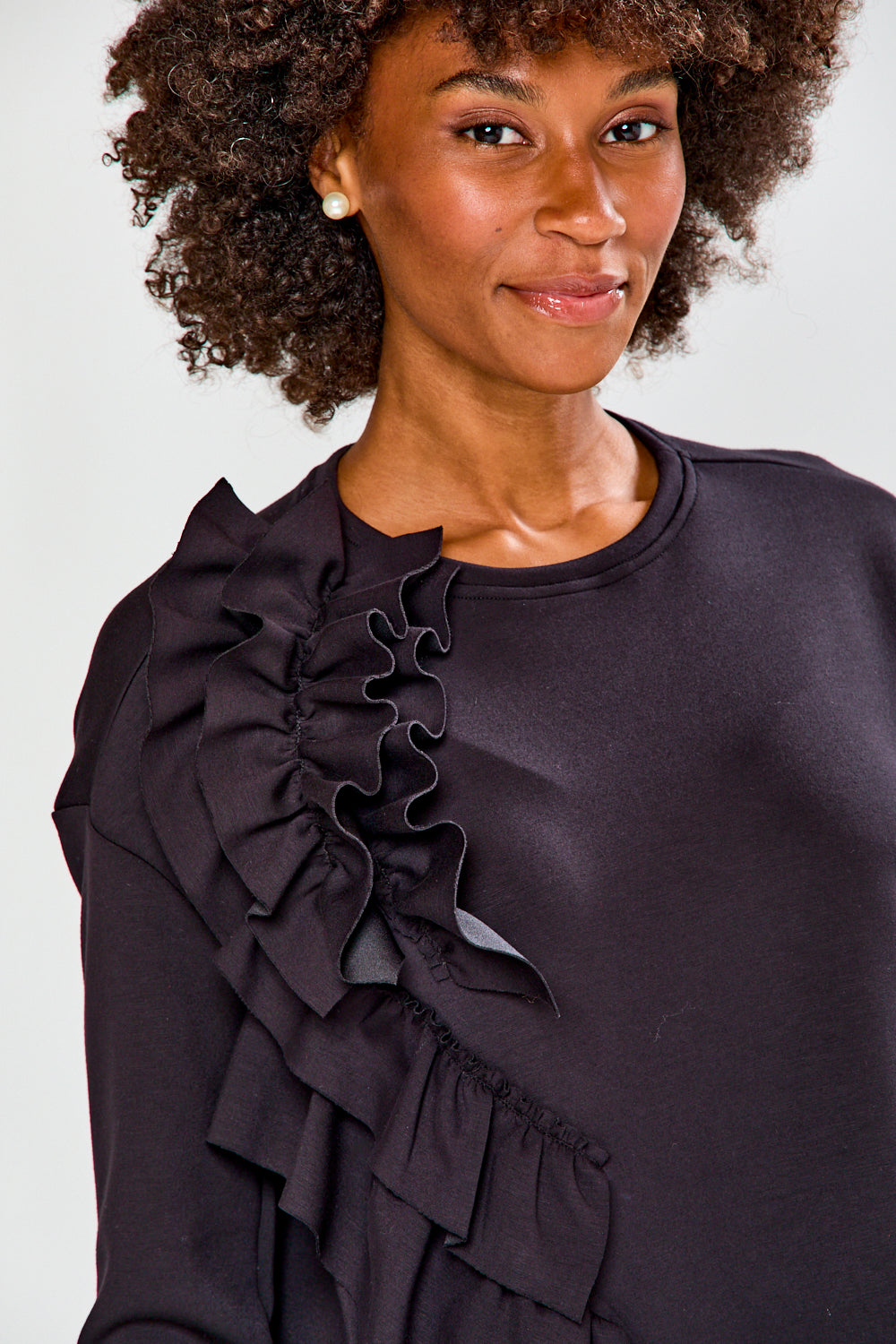 Woman wearing a black ruffled top and plaid pants against a white background
