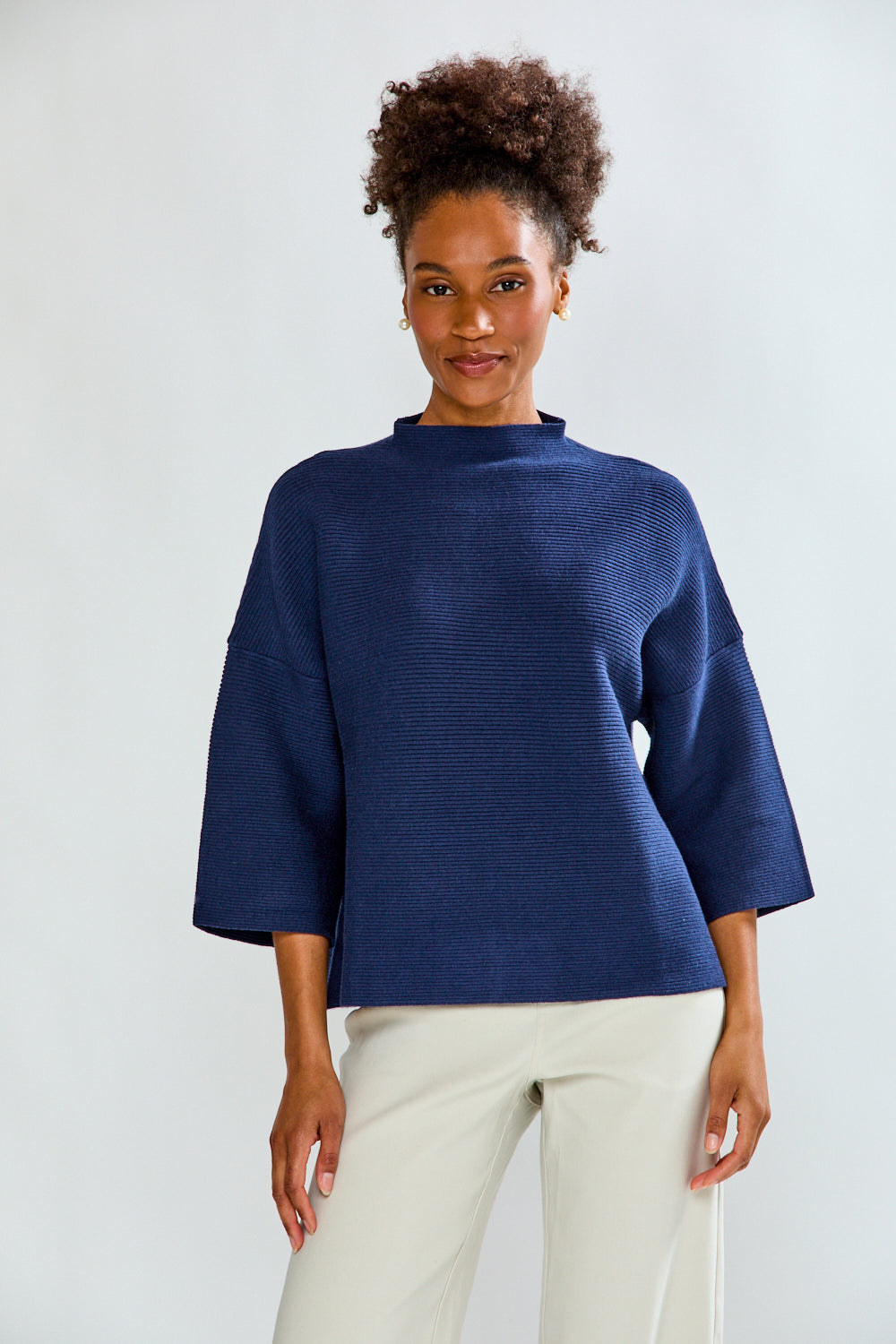 Woman wearing a blue textured top and white pants on a light gray background