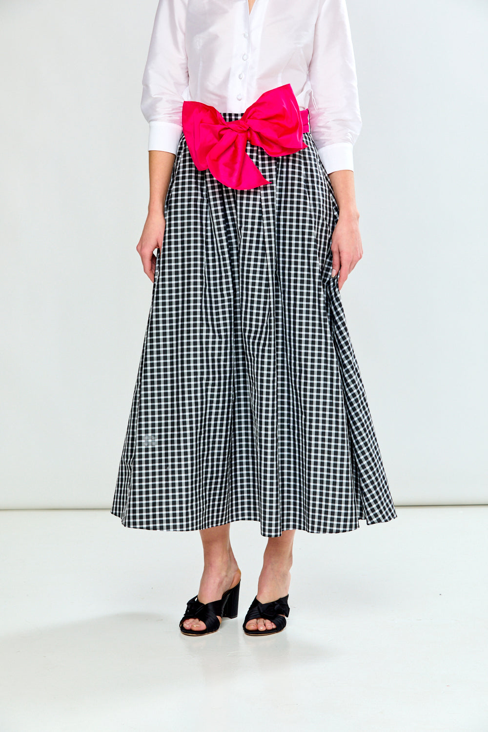 Person wearing a white shirt, black and white checkered skirt with a pink bow, and black sandals on a white background