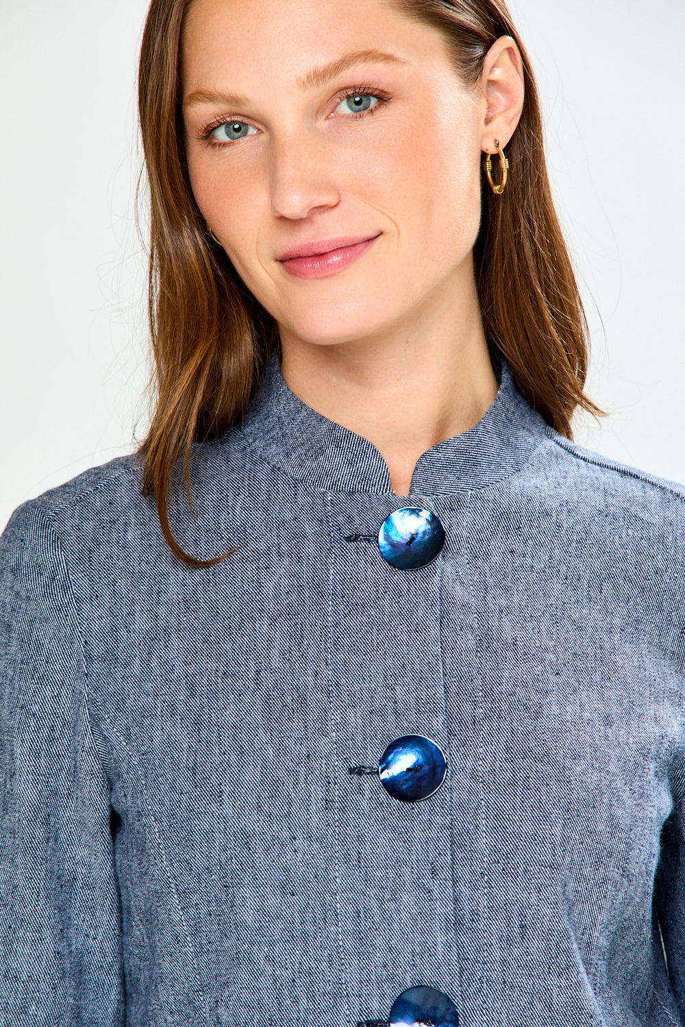 Woman wearing a gray coat with blue buttons against a white background