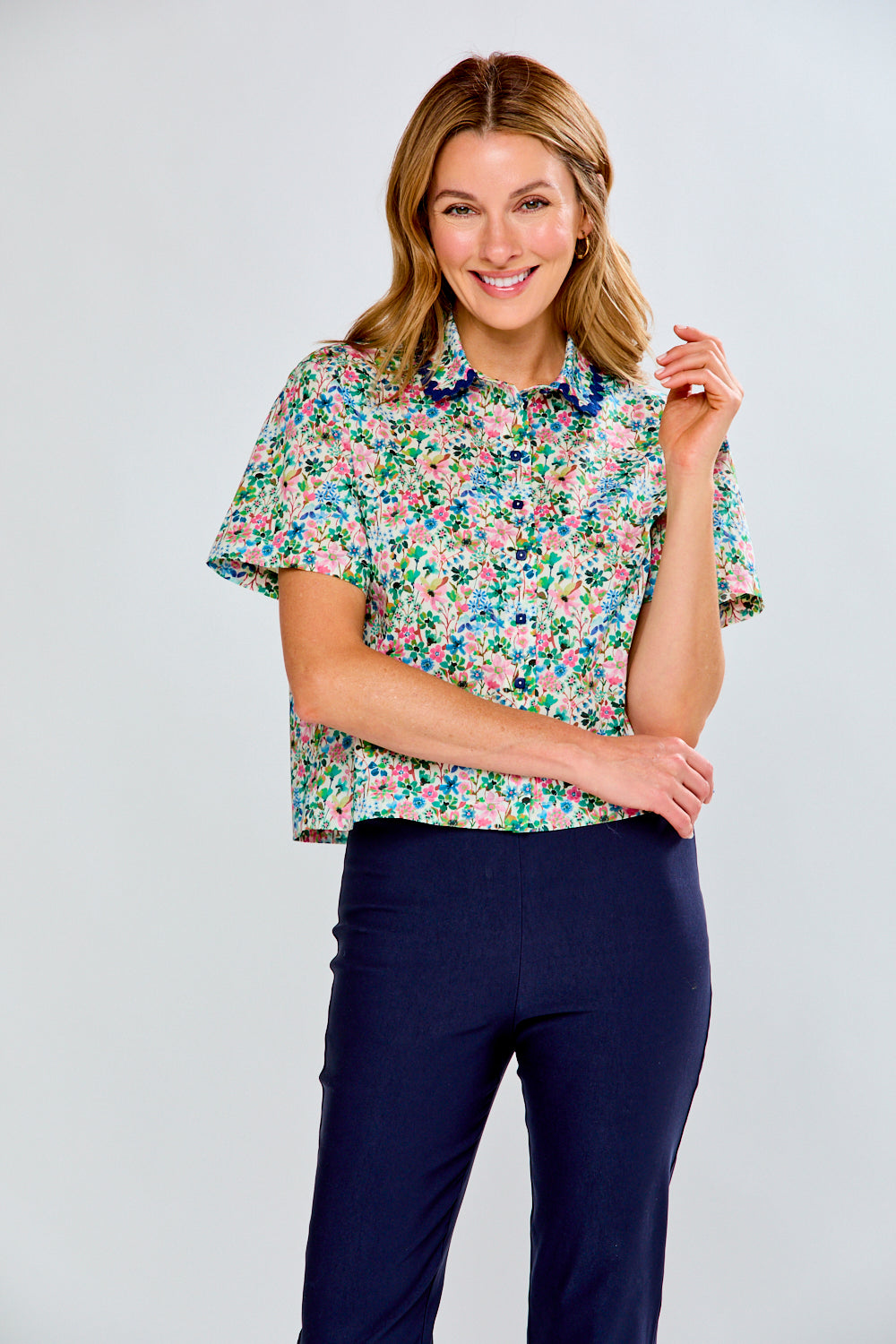 Woman wearing a floral blouse and navy pants against a light gray background