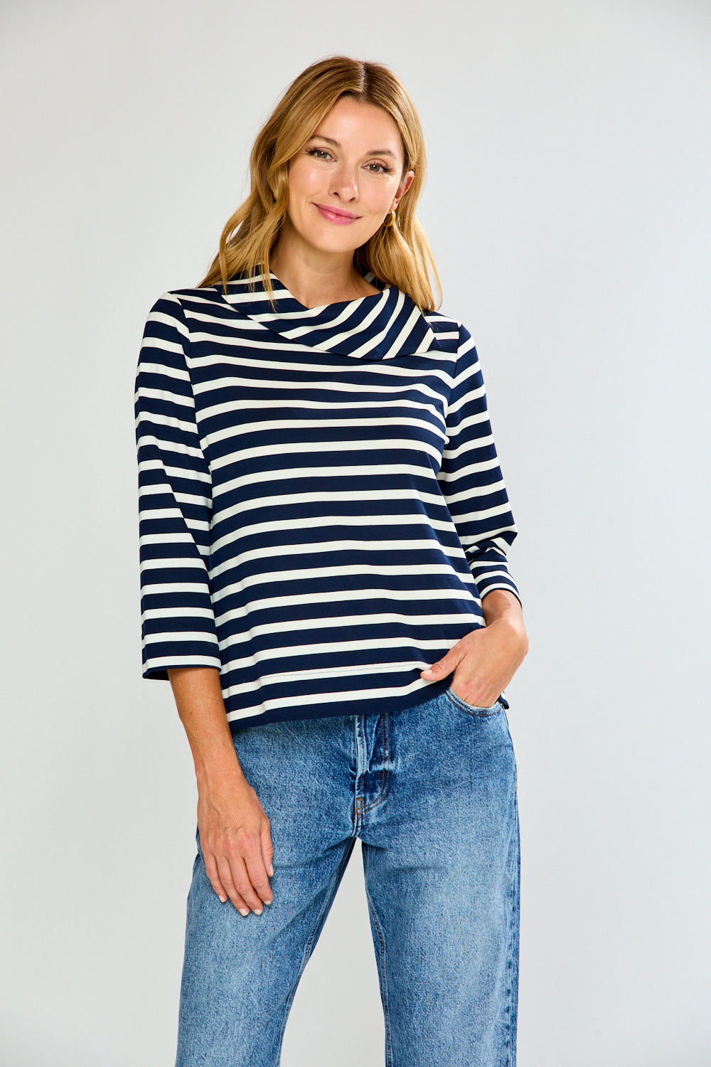 Woman wearing a navy and white striped sweater with blue jeans on a plain background