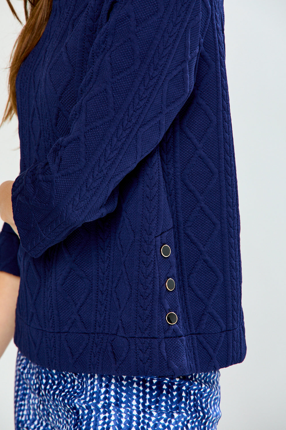 Woman wearing a navy blue cable knit top and patterned pants on a white background