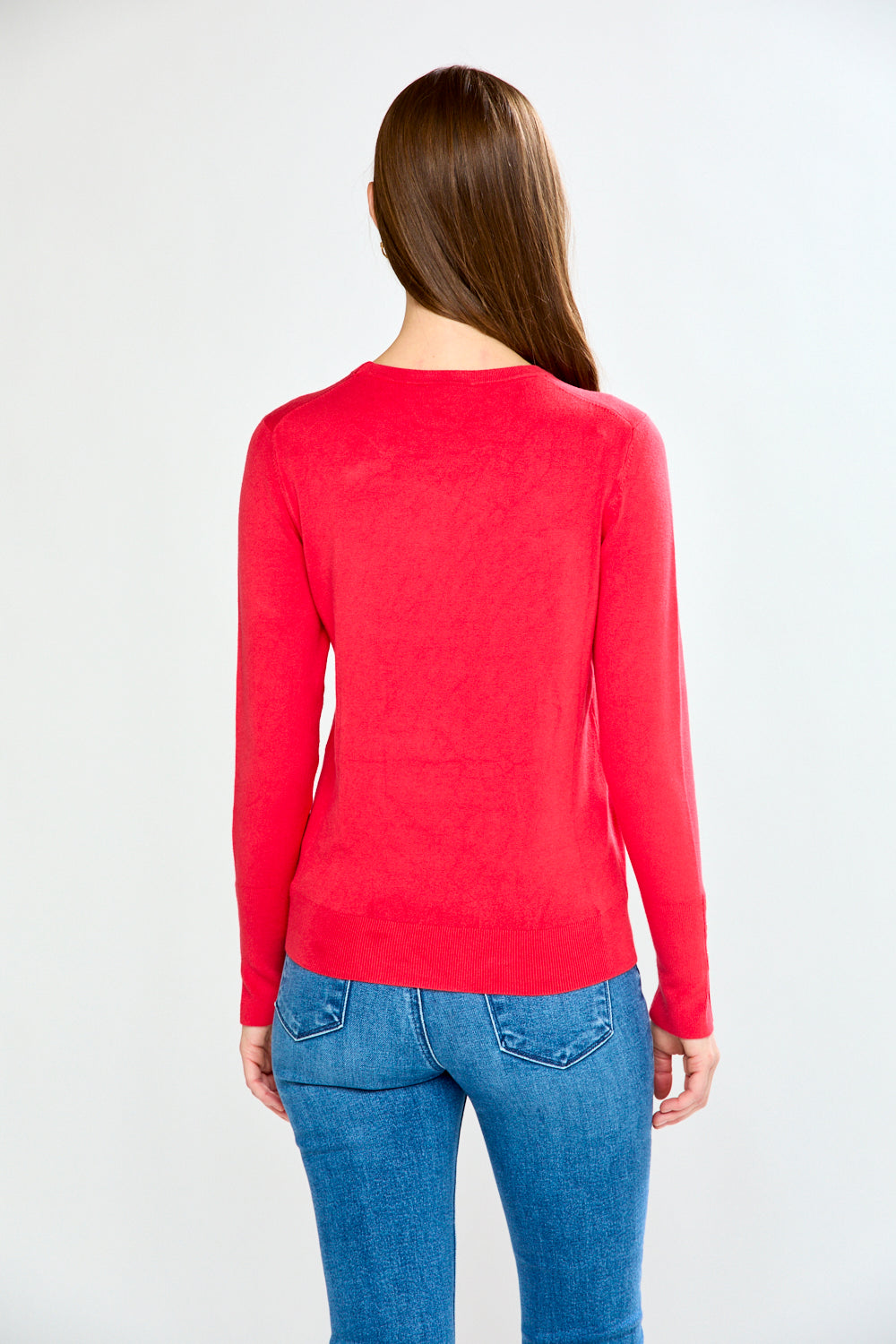Woman wearing a pink sweater and light blue jeans on a white background