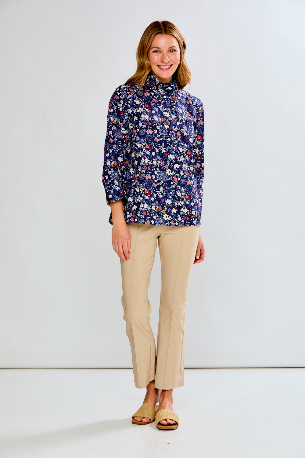 Woman wearing a floral blouse and beige pants on a white background