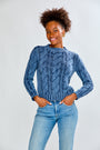 Woman wearing a denim cable knit sweater and blue jeans on a white background