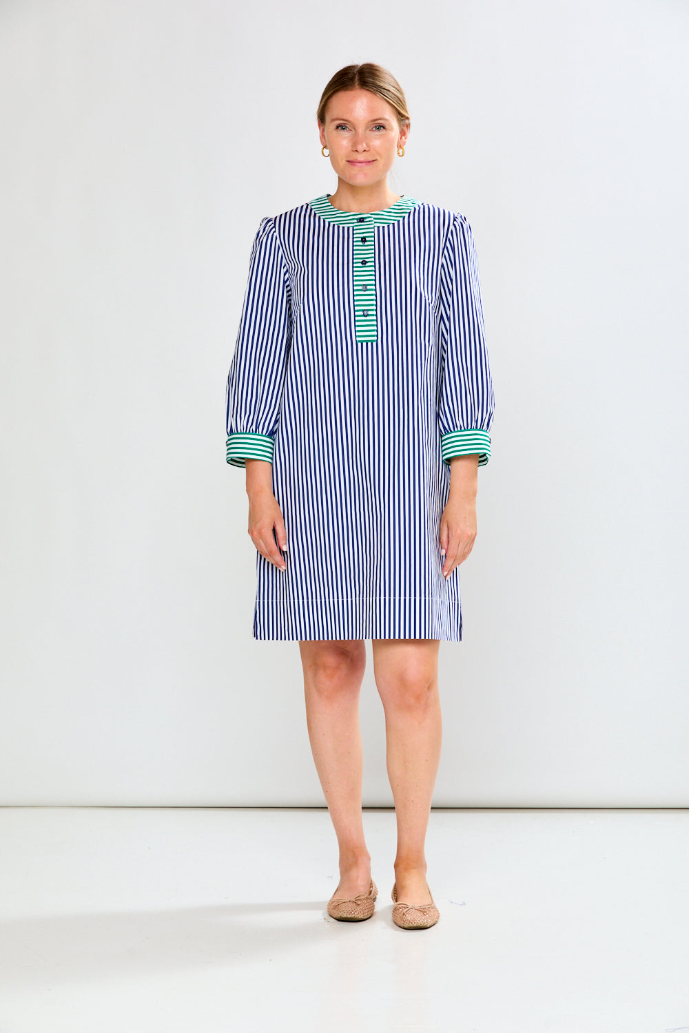 Woman wearing a blue and white striped dress with green accents on a white background