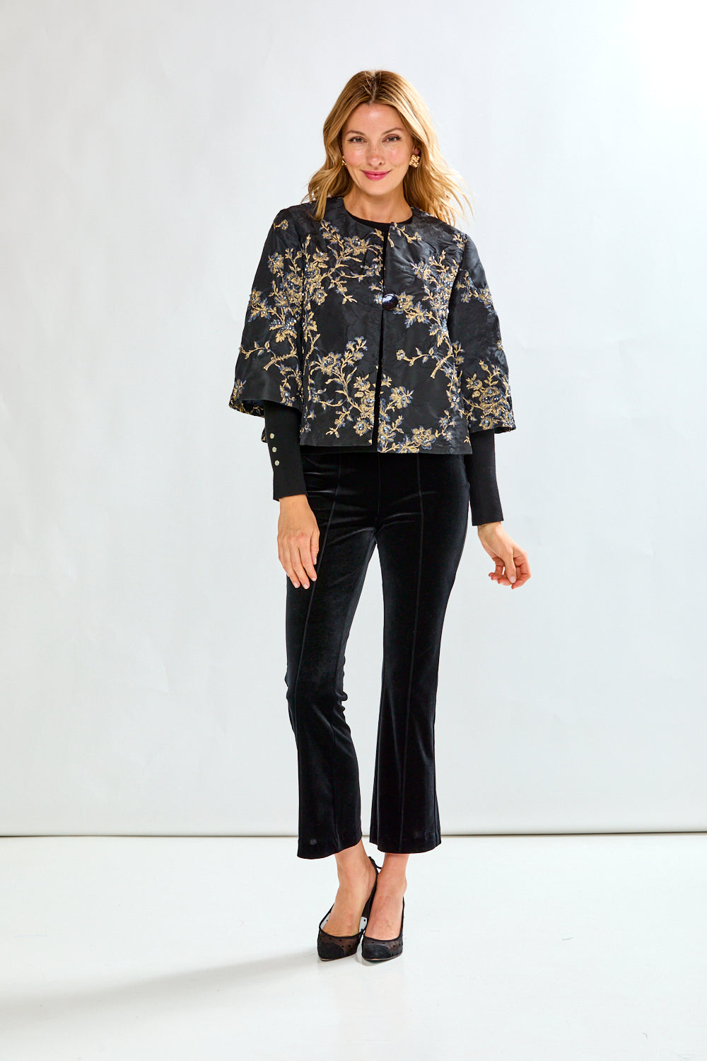 Woman wearing a black floral jacket and black pants on a white background