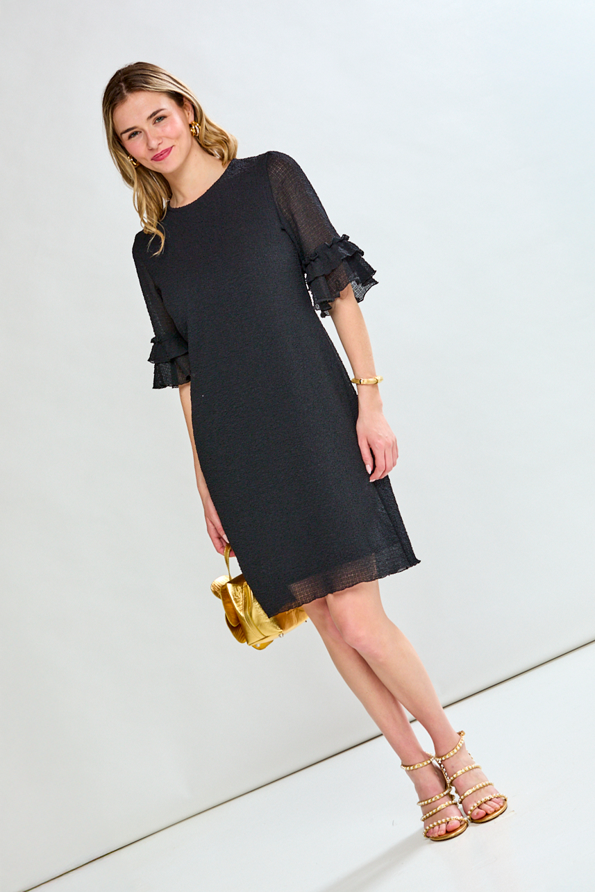 Woman wearing a black dress with sheer sleeves against a white background