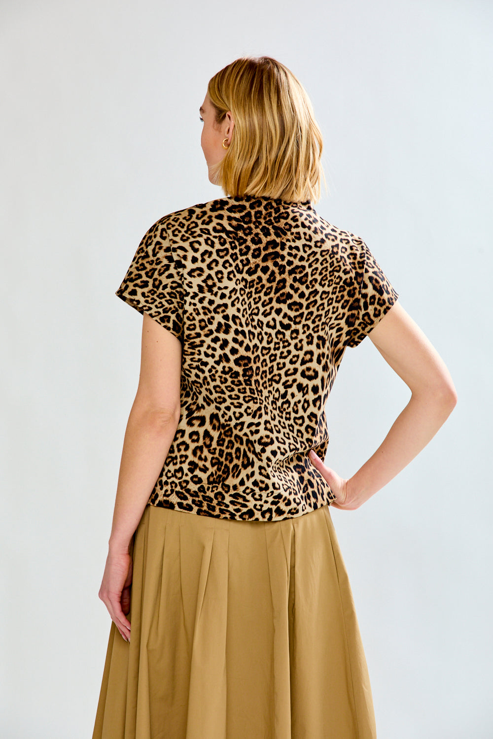 Woman wearing a leopard print top and beige skirt on a white background