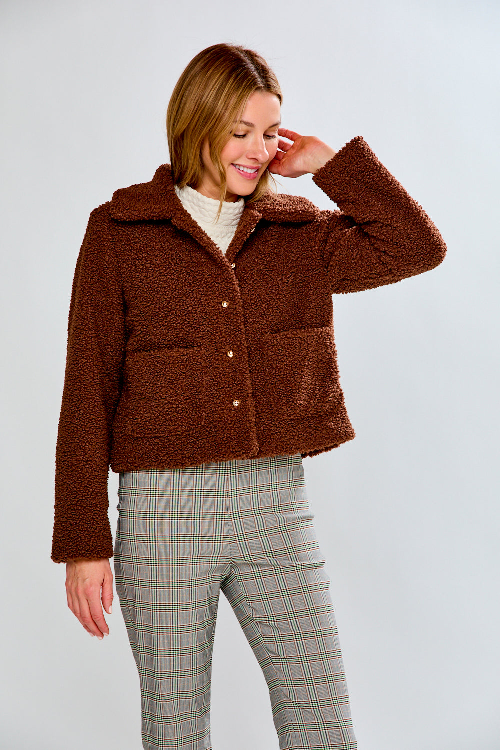 Woman wearing a brown jacket and plaid pants on a white background