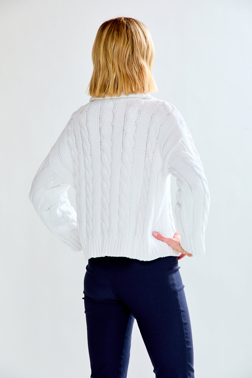Woman wearing a white cable knit sweater against a plain background