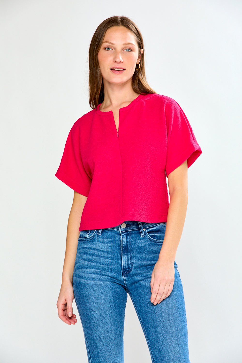 Woman wearing a bright pink top and blue jeans on a white background