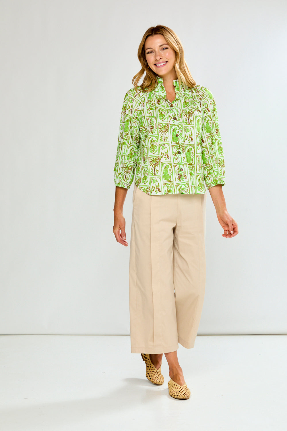 Woman wearing a green patterned blouse and beige pants on a white background