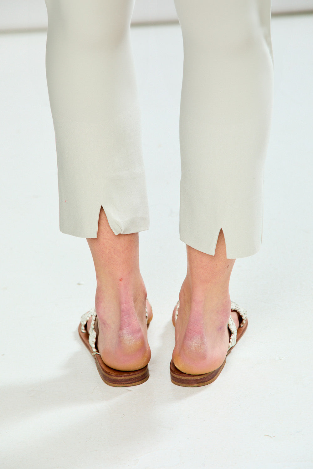 Person wearing beige pants and brown sandals on a white background