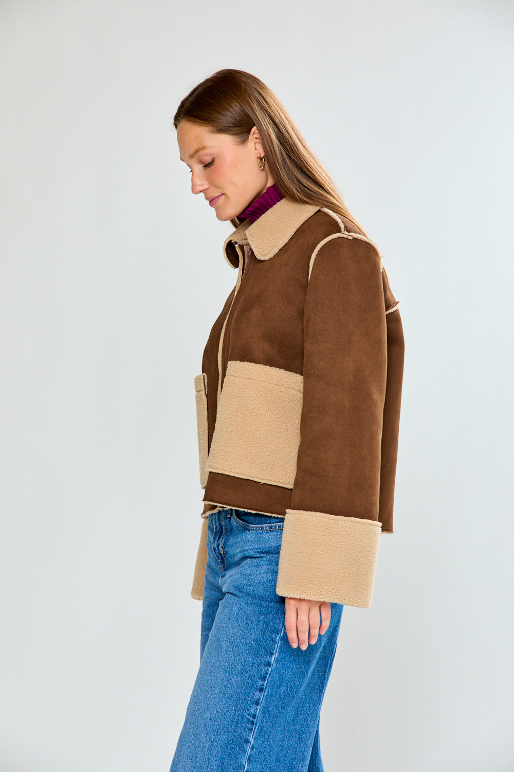 Woman wearing a brown and beige jacket with blue jeans on a white background