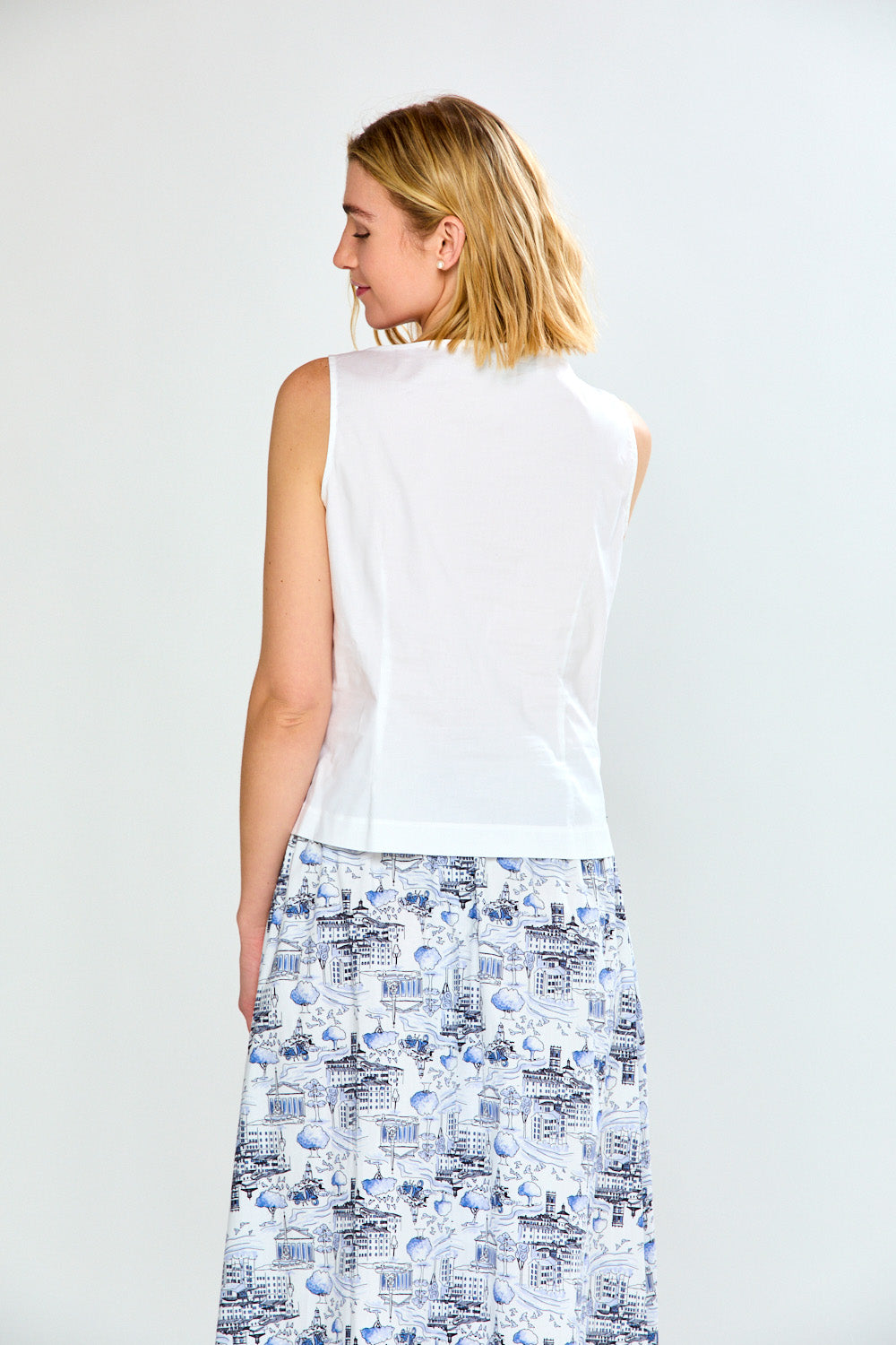 Woman wearing a white sleeveless top and patterned skirt on a plain background