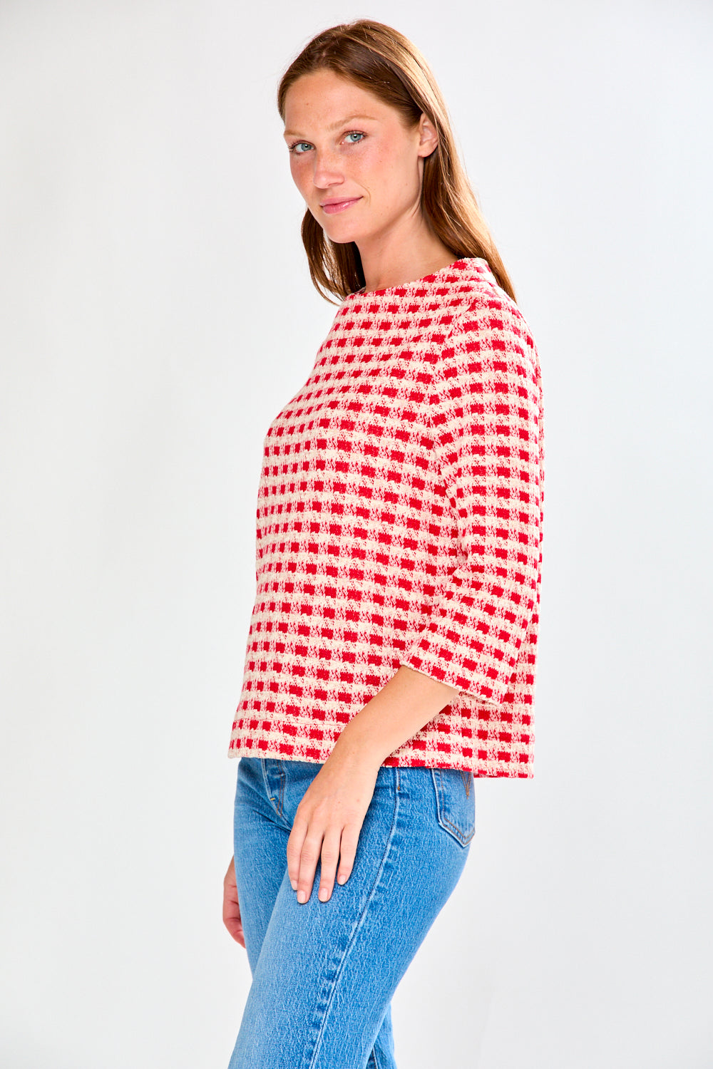 Woman wearing a red and white checkered shirt with blue jeans on a white background