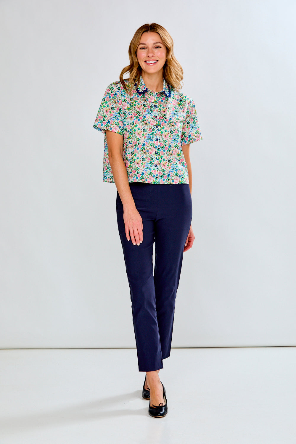 Woman wearing a floral blouse and navy pants on a white background