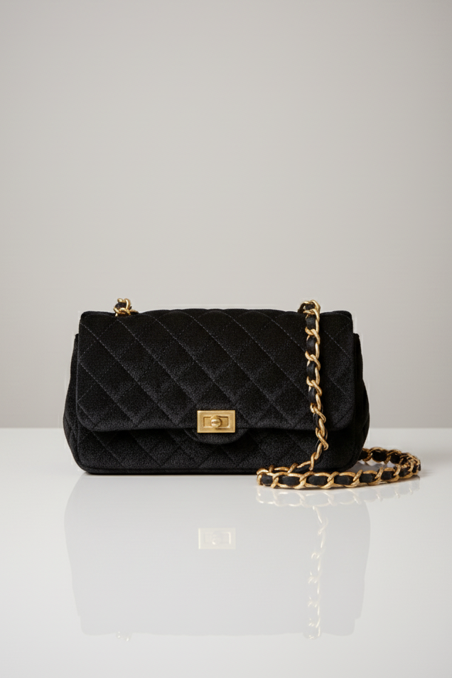 Black quilted handbag with gold chain on a white surface and light gray background