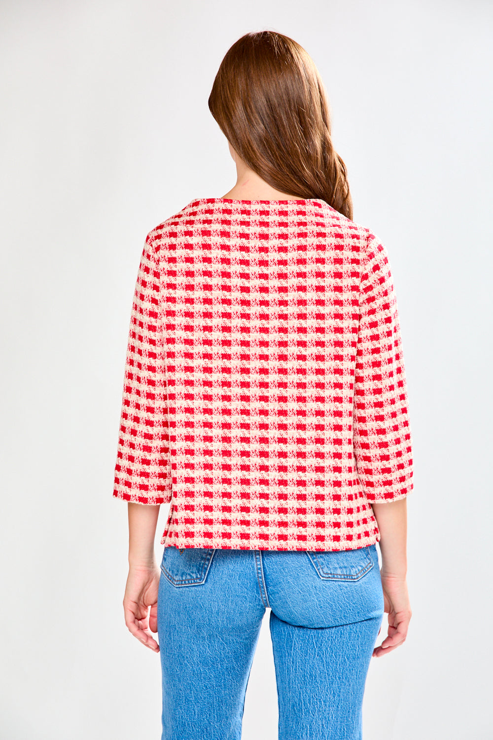 Woman wearing a red and white checkered shirt with blue jeans on a white background