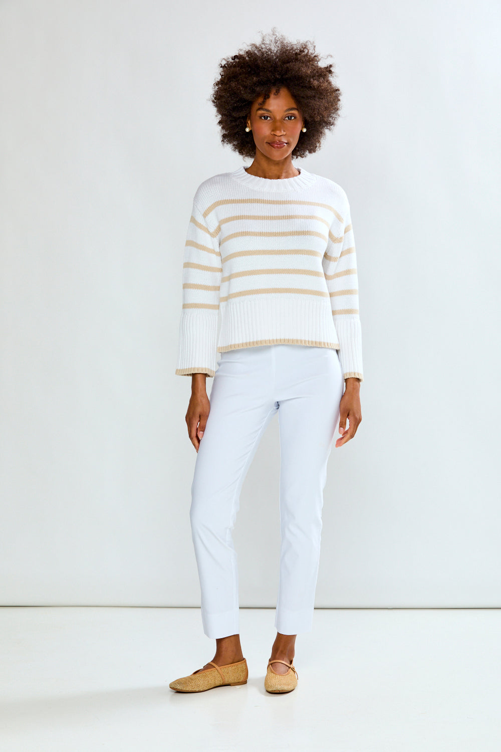 Woman wearing a white and gold striped sweater with white pants on a white background