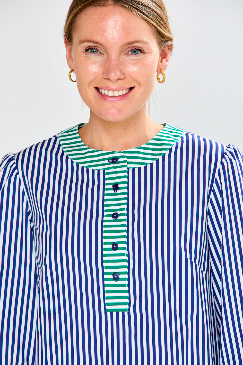 Woman wearing a blue and white striped shirt with a green and white striped collar against a light gray background