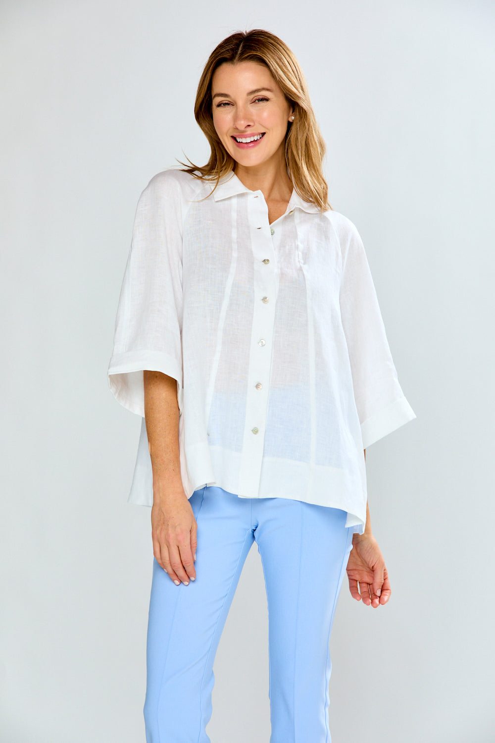 Woman wearing a white blouse and light blue jeans against a plain background
