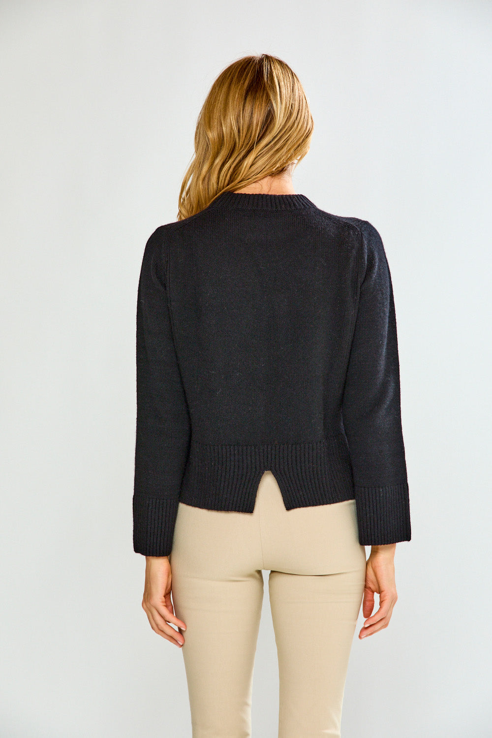 Woman wearing a black sweater and beige pants against a white background