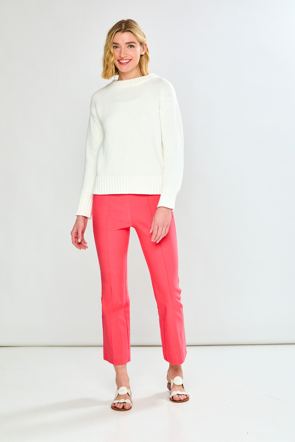 Woman wearing a white sweater and pink pants against a white background
