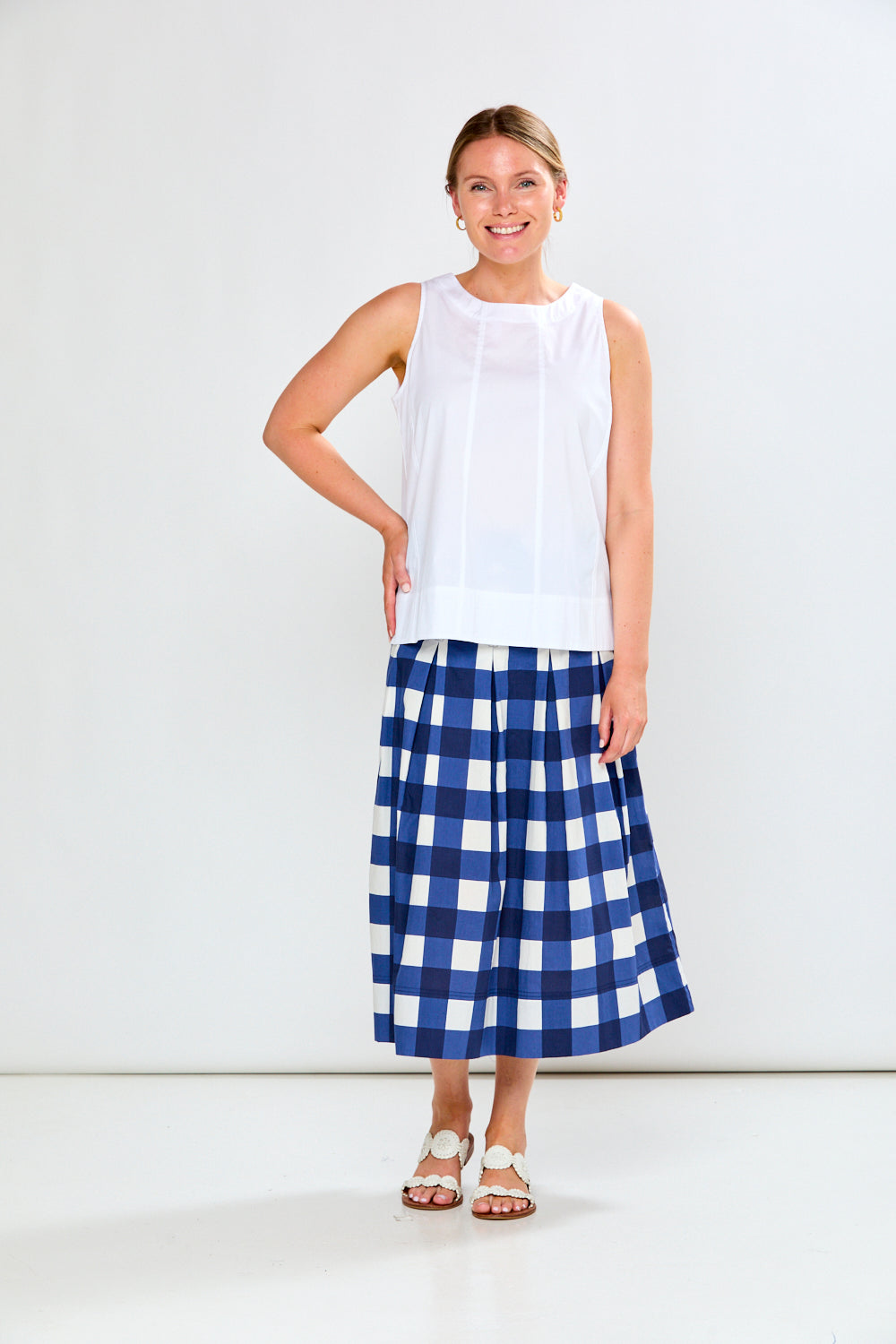 Woman wearing a white sleeveless top and blue plaid skirt on a white background