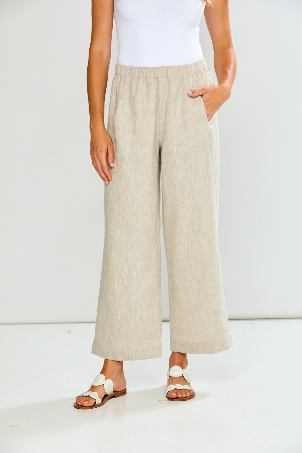 Person wearing beige wide-leg pants and white sandals on a plain background