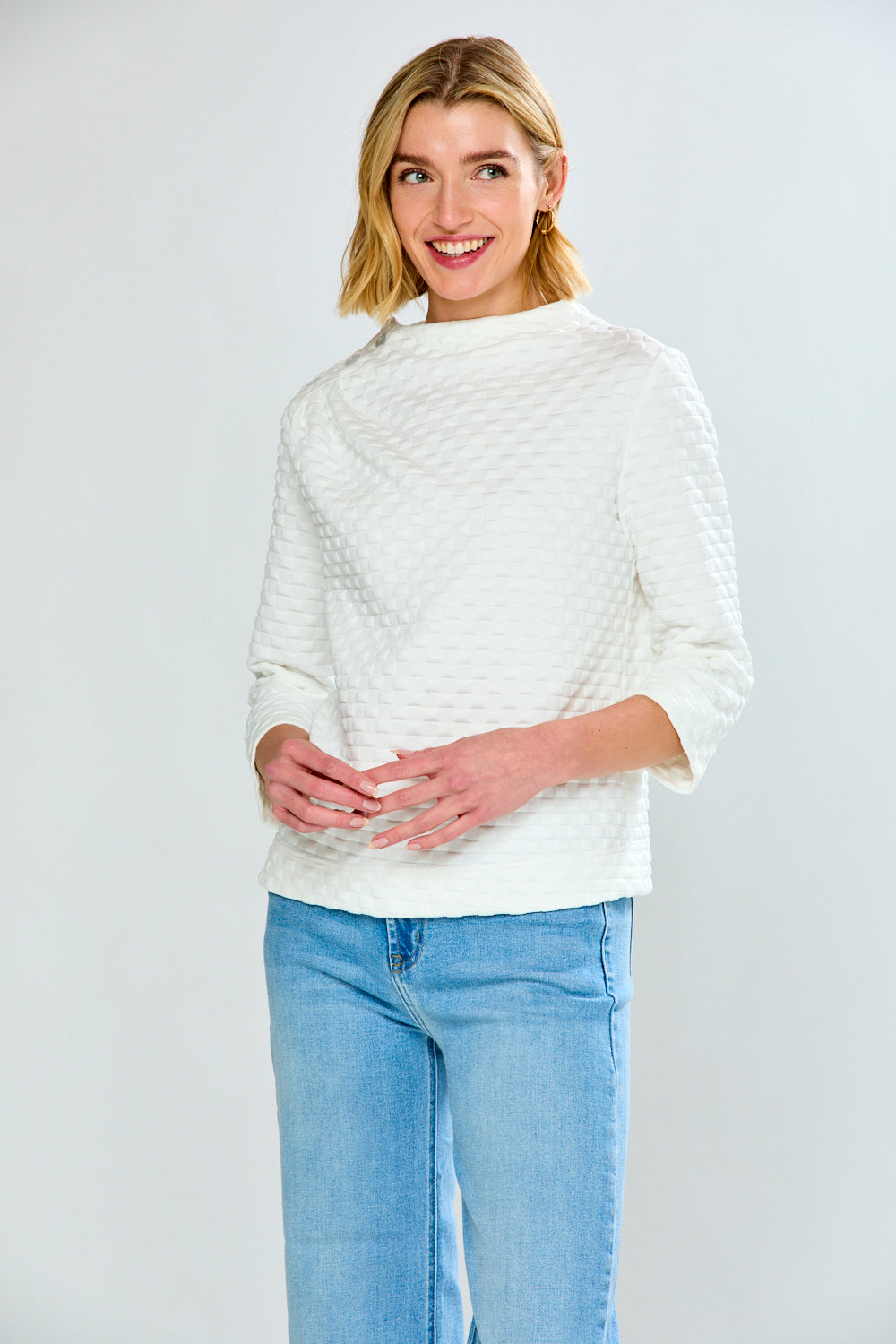 Woman wearing a white textured sweater and light blue jeans on a plain background