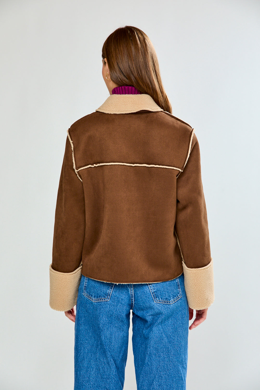 Woman wearing a brown and beige jacket with blue jeans on a white background