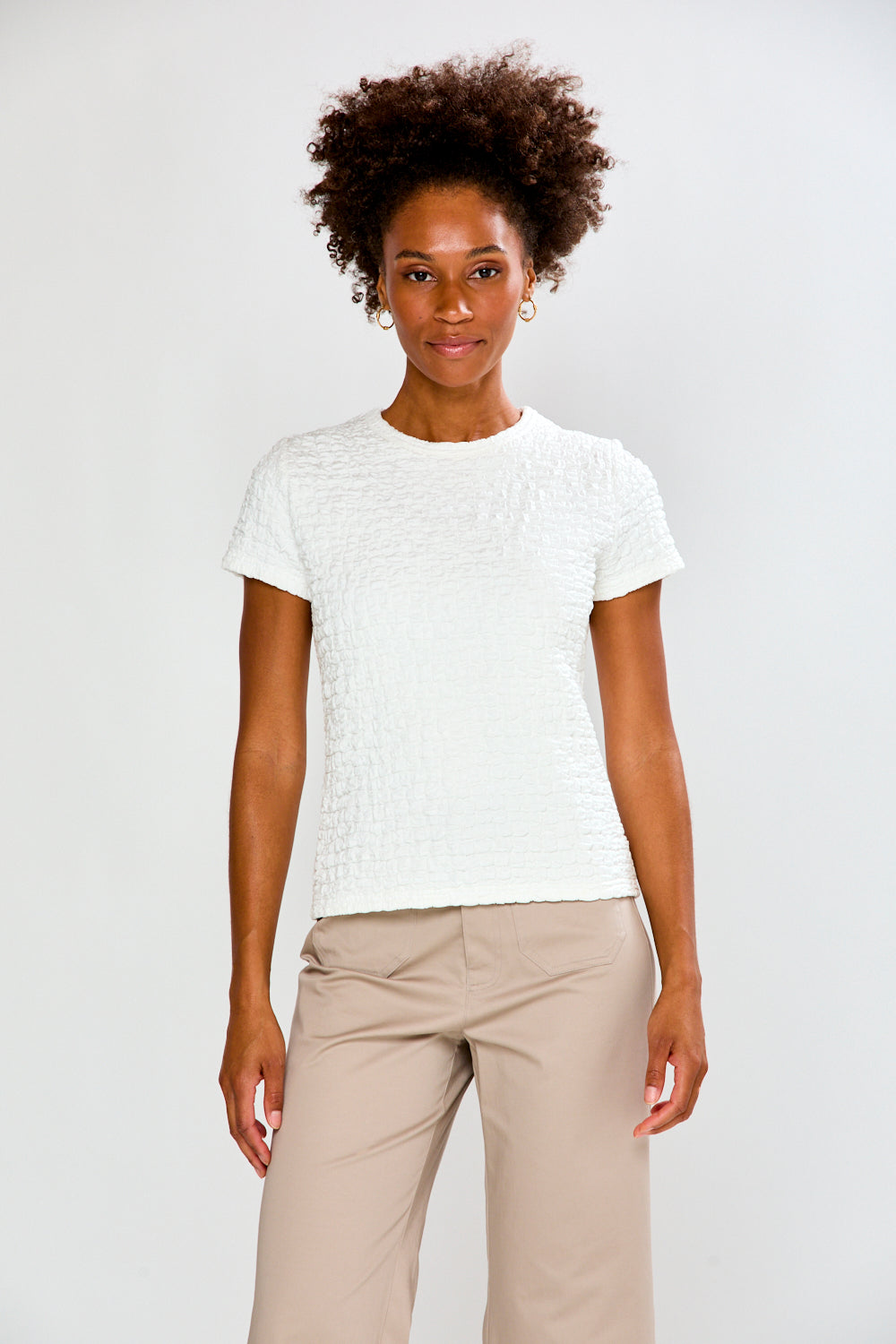 Woman wearing a white textured shirt and beige pants on a plain background
