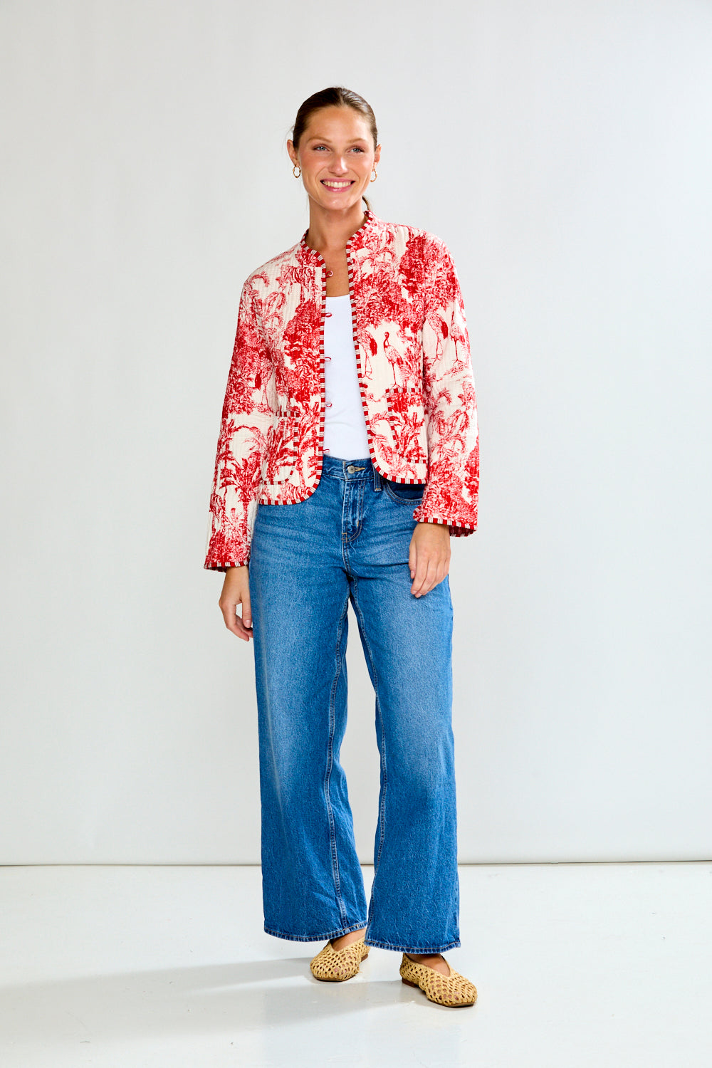 Woman wearing a red floral jacket and blue jeans on a white background