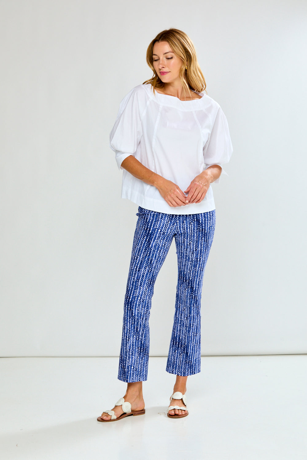 Woman wearing a white blouse and blue patterned pants on a plain background