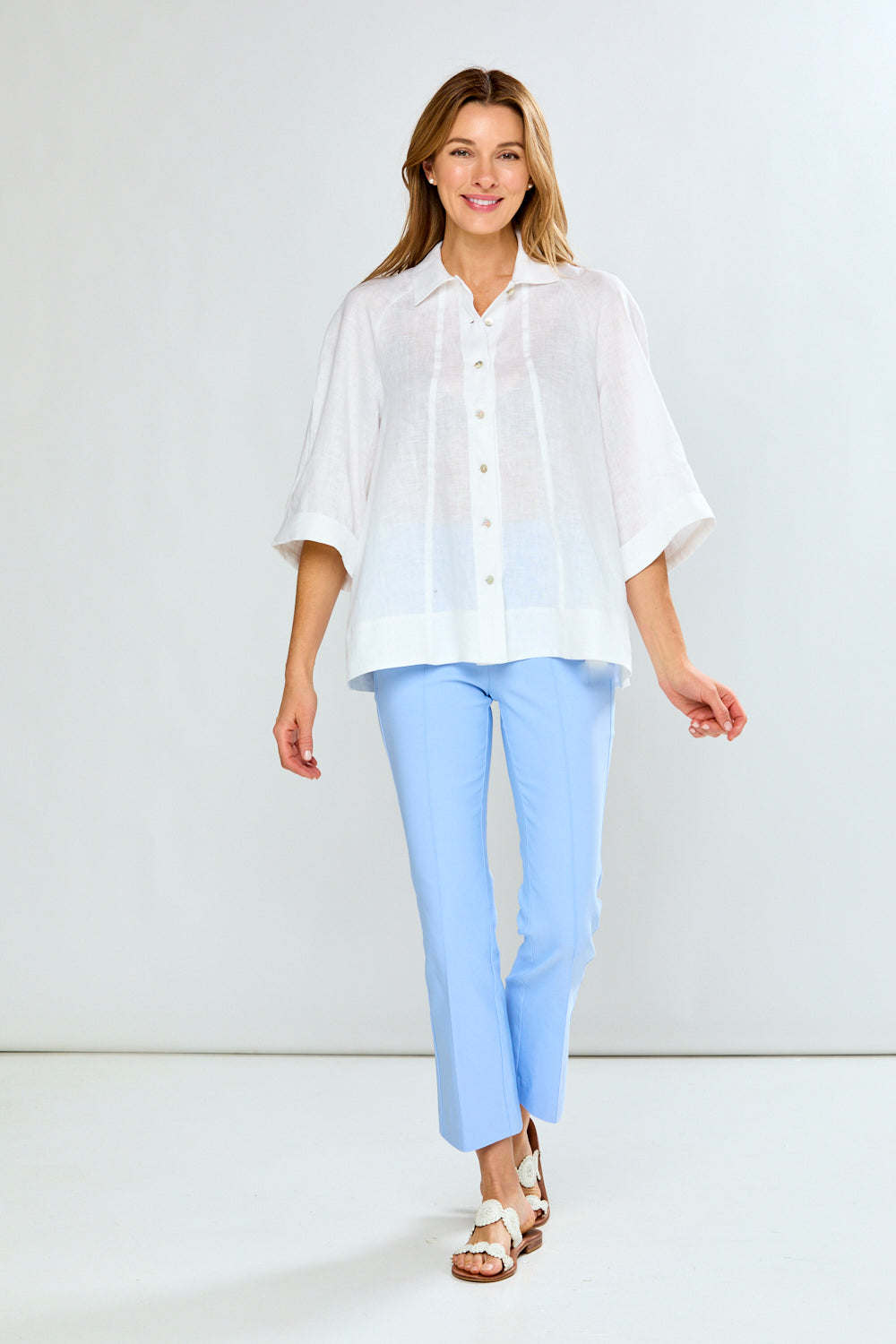 Woman wearing a white blouse and light blue pants against a white background