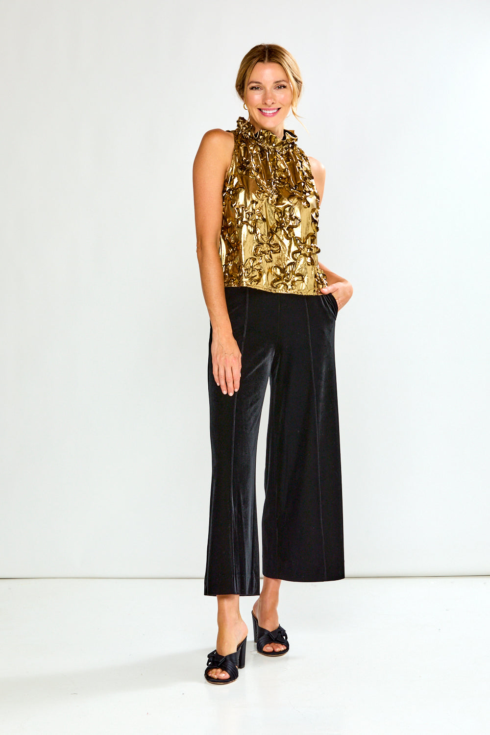 Woman wearing a gold metallic top and black pants on a white background