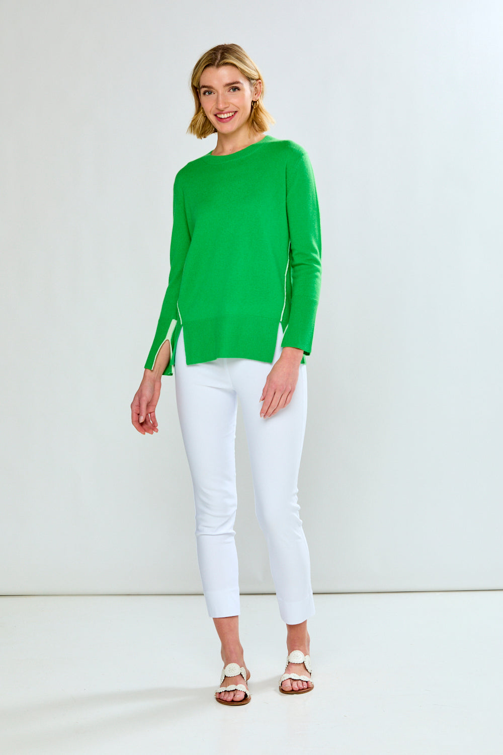 Woman wearing a green sweater and white pants against a white background