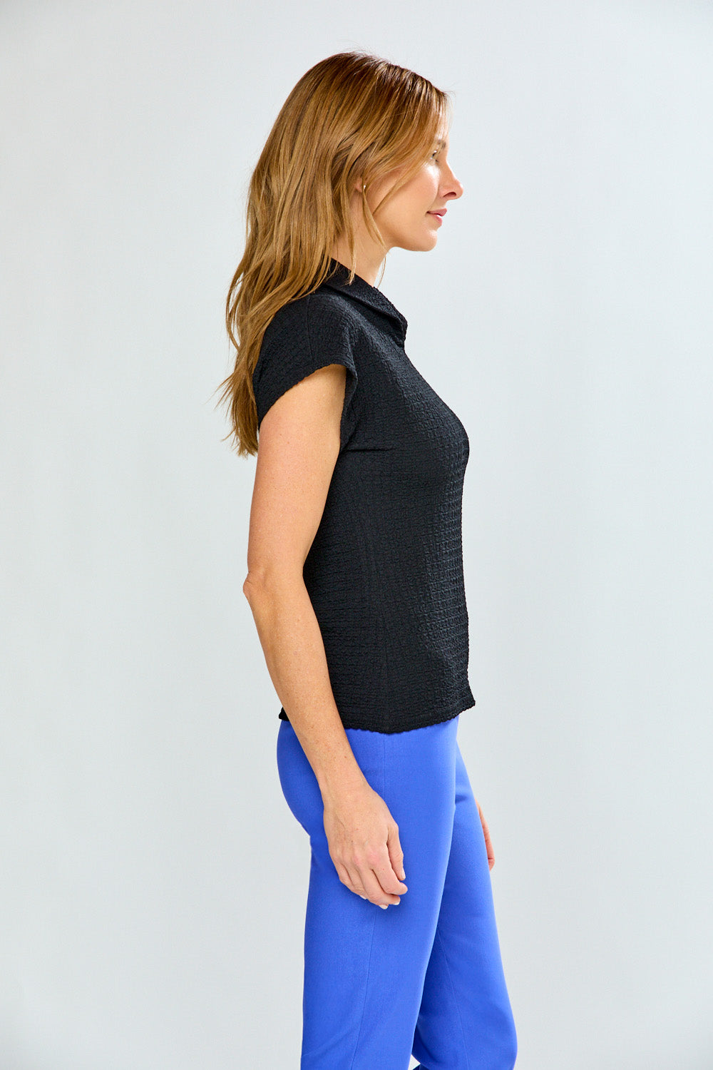 Woman wearing a black sleeveless top and blue pants on a light gray background