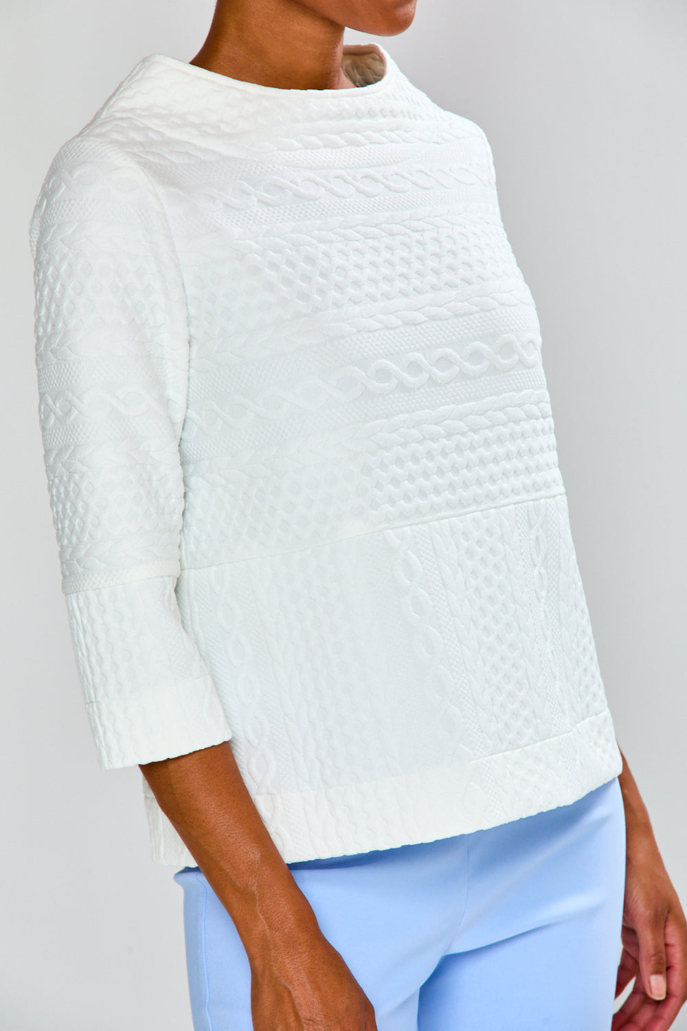 White textured sweater worn by a person on a gray background