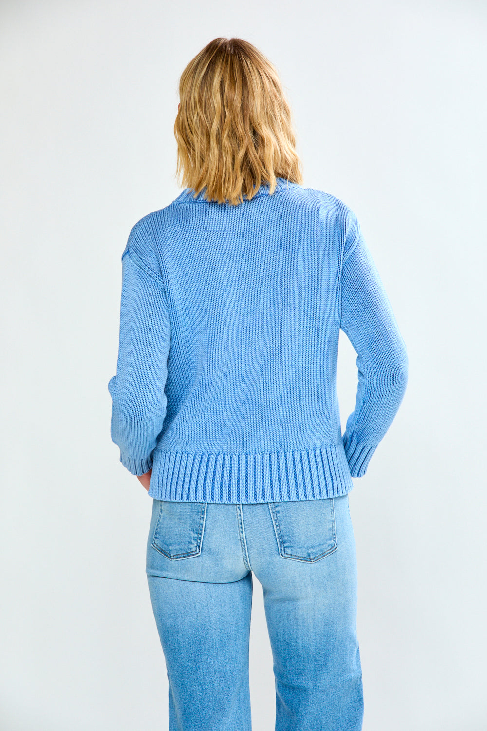 Woman wearing a blue sweater and light blue jeans on a white background