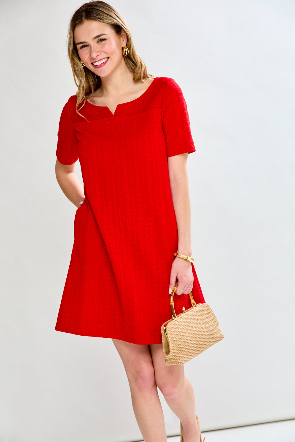 Woman wearing a red dress holding a beige handbag against a white background