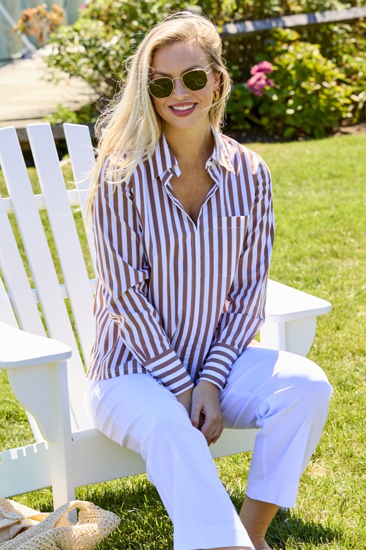 Woman wearing a striped shirt and sunglasses sitting on a white chair outdoors.