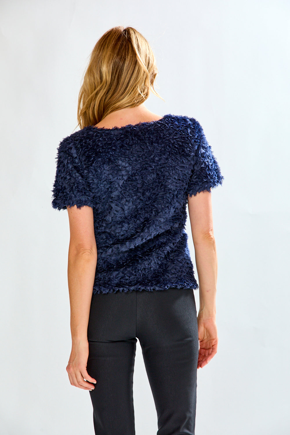 Woman wearing a textured navy blue top and black pants on a white background