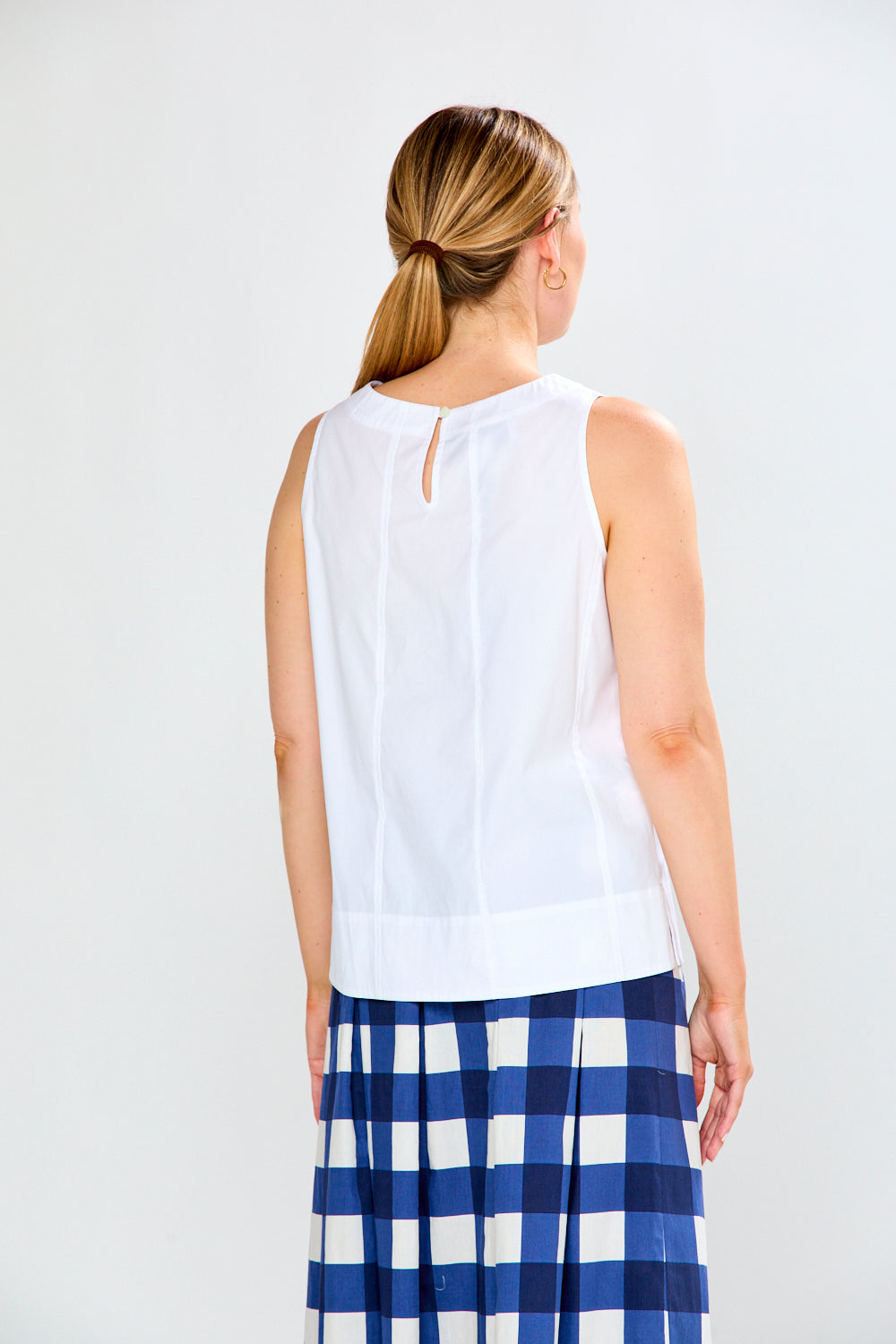 Woman wearing a white sleeveless top and blue plaid skirt on a white background