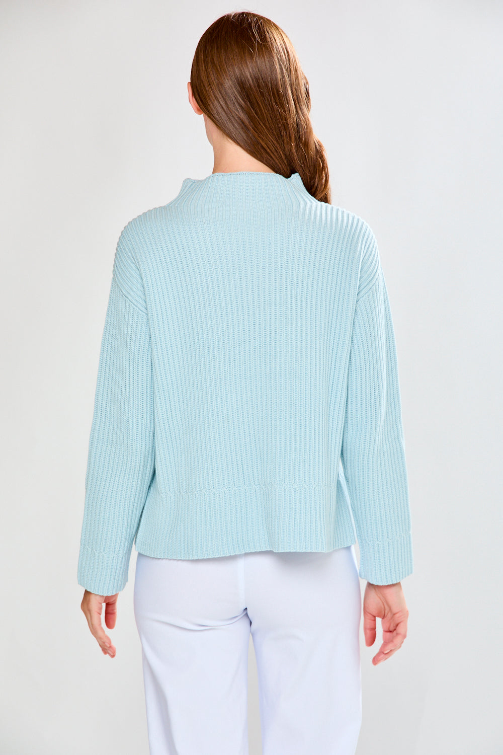 Woman wearing a light blue ribbed sweater and white pants on a plain background