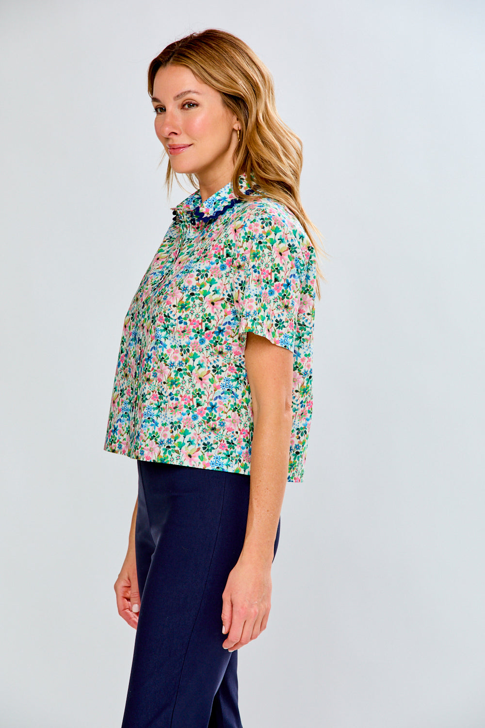 Woman wearing a floral blouse and dark pants on a white background